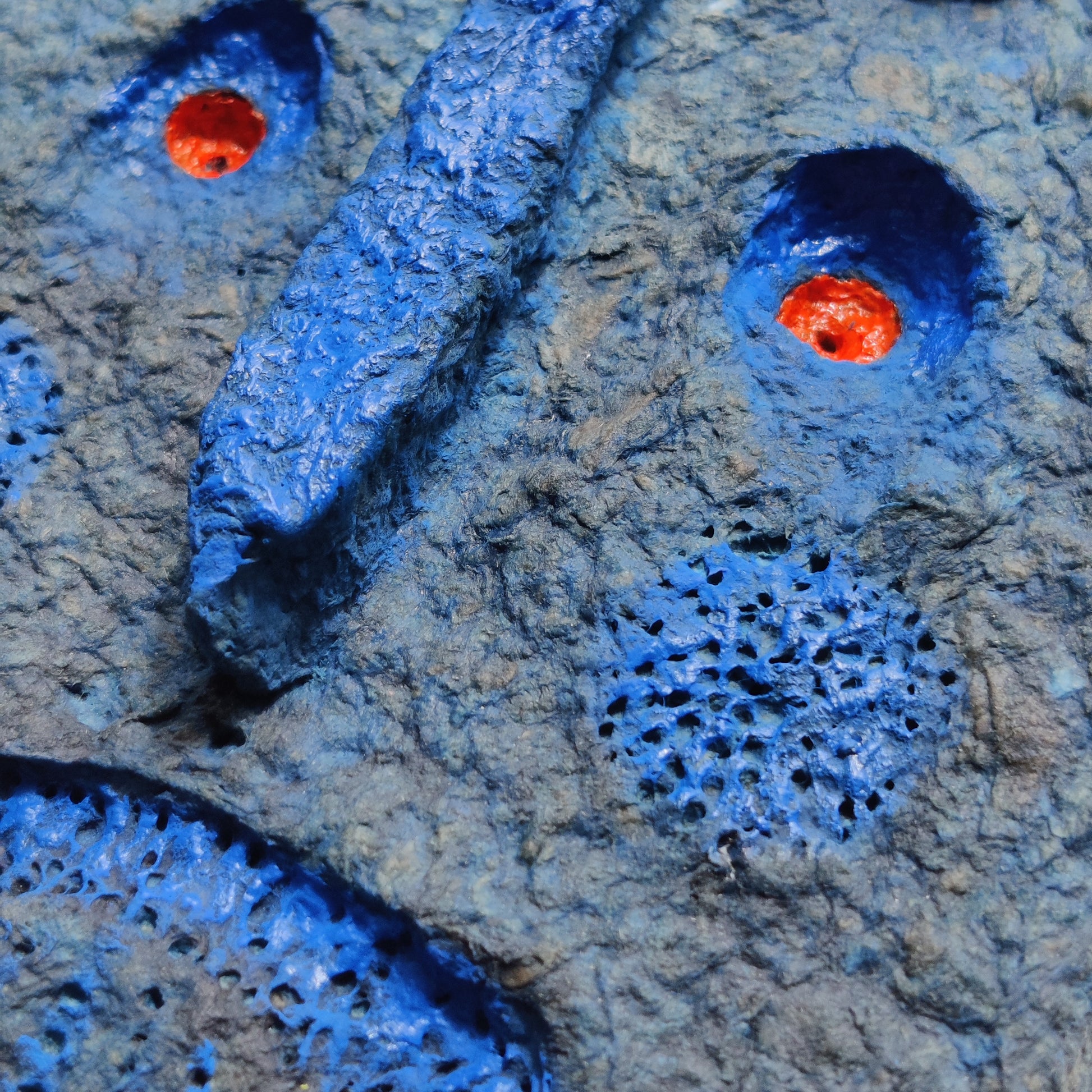 Close-up of textured blue and gray paper clay mask e with red circular eyes