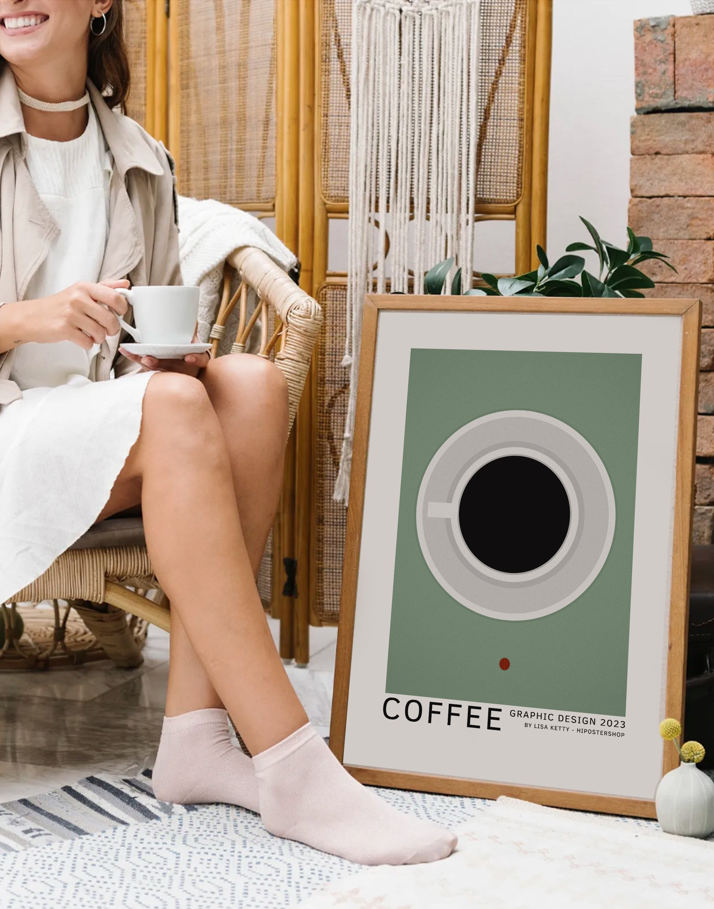 Woman sitting on a chair holding a cup of coffee next to a framed coffee graphic design print.
