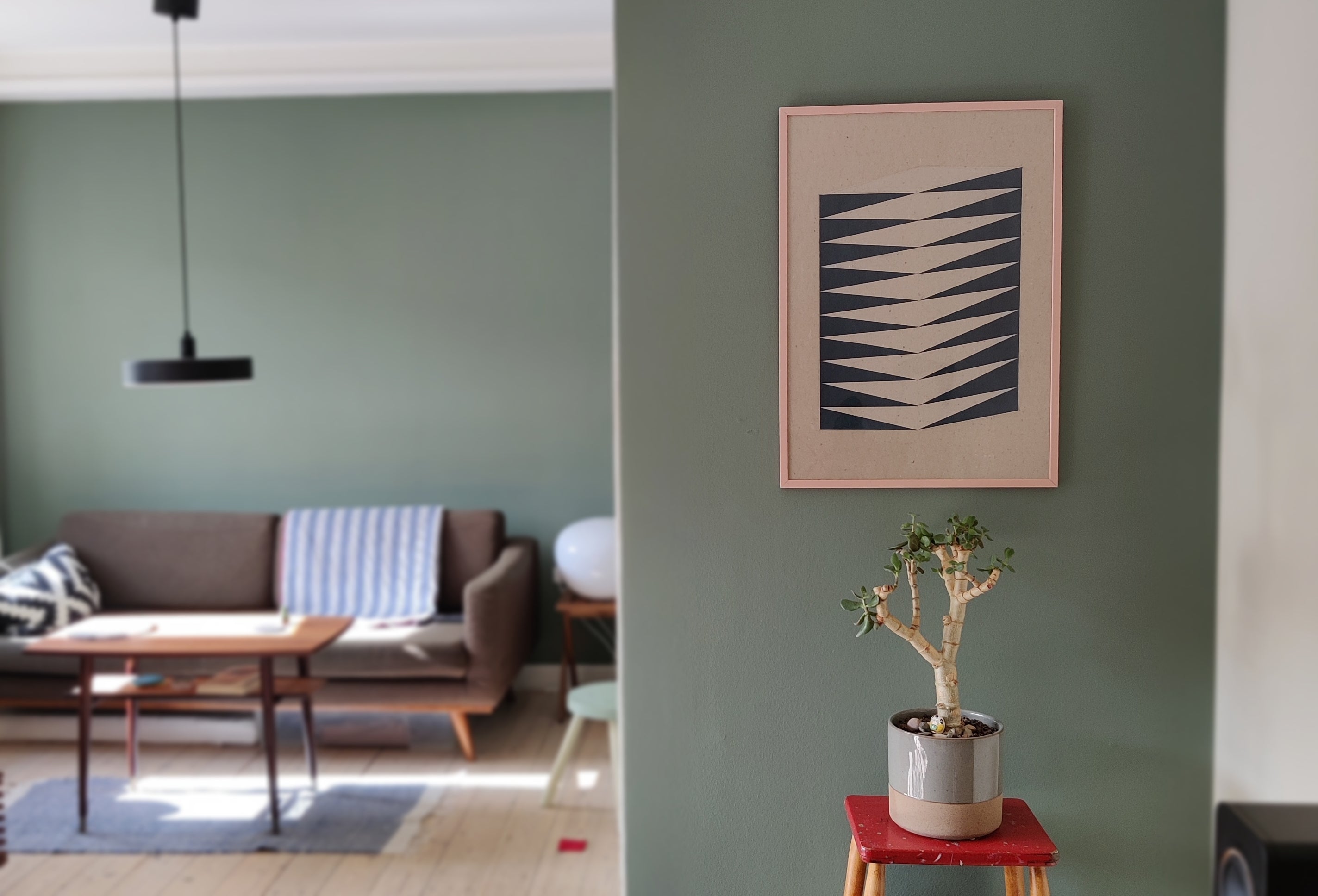 Living room with a green wall, sofa, coffee table, and decorative plant and my artwork I call Fishbone.