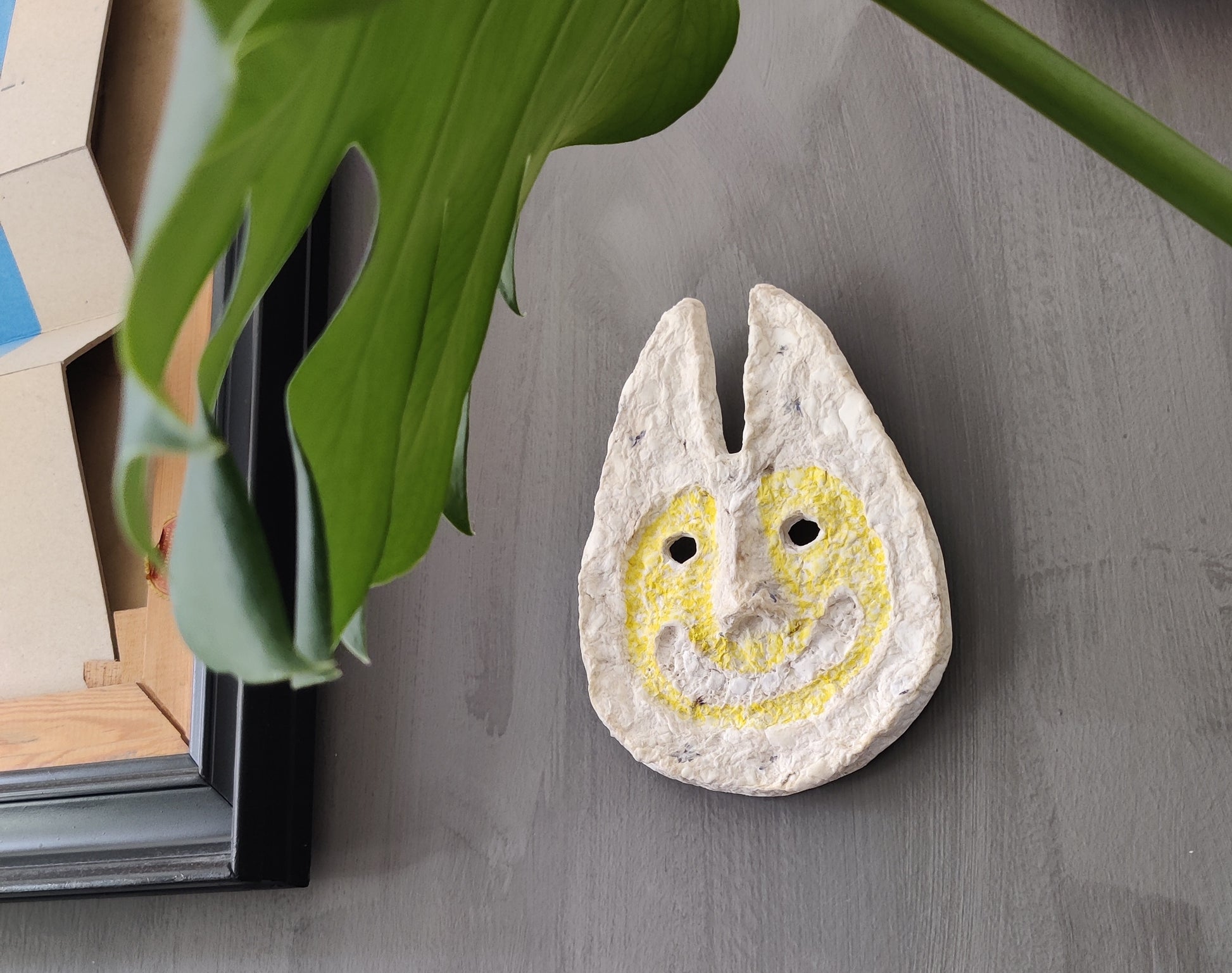 Decorative stone with a smiley face design on a gray surface with a plant in the background